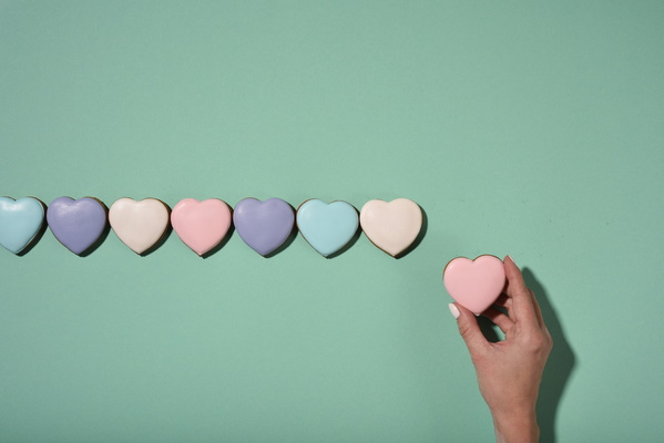 Multicolored Heart-Shaped Cookies Lie in Line and Girl Holding One Of Them